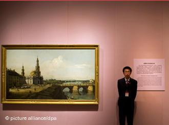 	Ein Sicherheitsmitarbeiter steht am Freitag (01.04.2011) in Peking im National Museum of China in der Ausstellung "Die Kunst der Aufklärung" zwischen den Gemälden "Das historische Dresden" von Bernardo Bellotto (Canaletto) aus dem Jahr 1748 Staatliche Kunstsammlungen Dresden (l) und "Selbstporträt des Knstlers mit seiner Tochter Antonia" von Georg Desmarees, ca. 1760, Alte Pinakothek Mnchen. Bundesaußenminister Westerwelle (FDP) eröffnete die Ausstellung, die von den Staatlichen Museen in Berlin, Mnchen und Dresden vorbereitet wurde. Das Museum gilt als das derzeit größte Museum der Welt. Foto: Arno Burgi dpa
